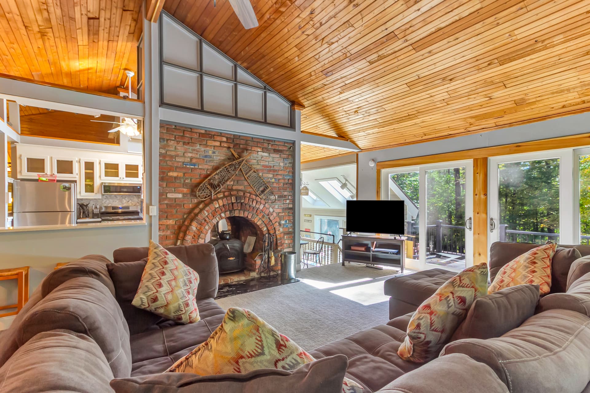 Gill Terrace great room with vaulted pine ceiling, brick fireplace, and views to the deck