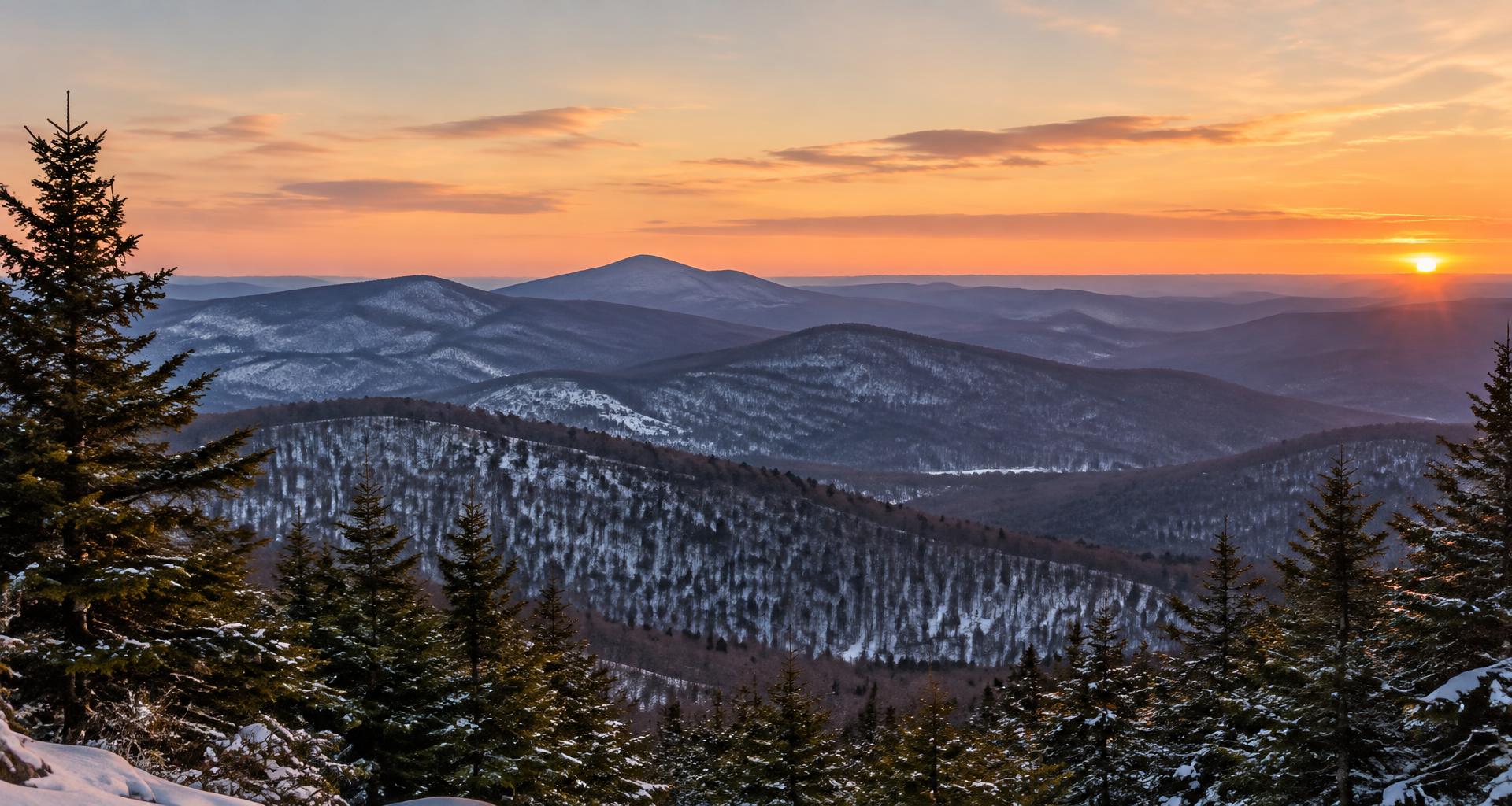 Snow-dusted Vermont mountain ridges beneath a warm sunset